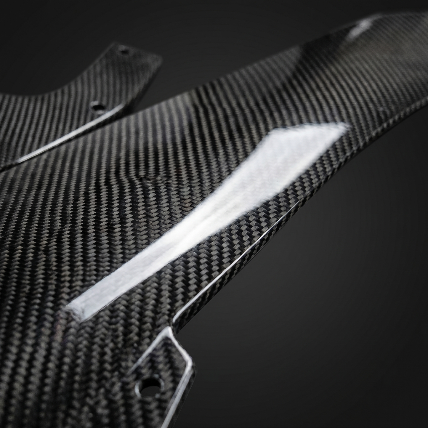 Macro of gloss 2x2 twill dry carbon weave on BMW M3 front lip edge, light-bar reflection showing clear-coat depth and machined edge