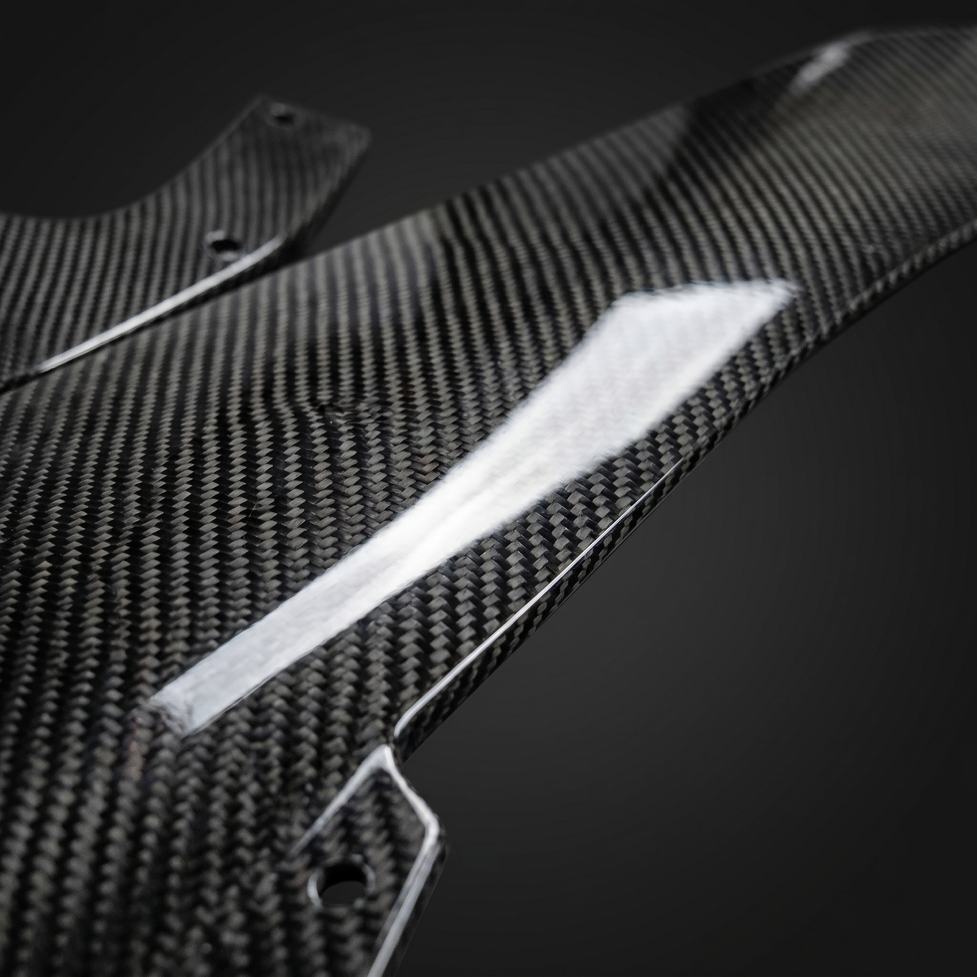 Macro of gloss 2x2 twill dry carbon weave on BMW M3 front lip edge, light-bar reflection showing clear-coat depth and machined edge