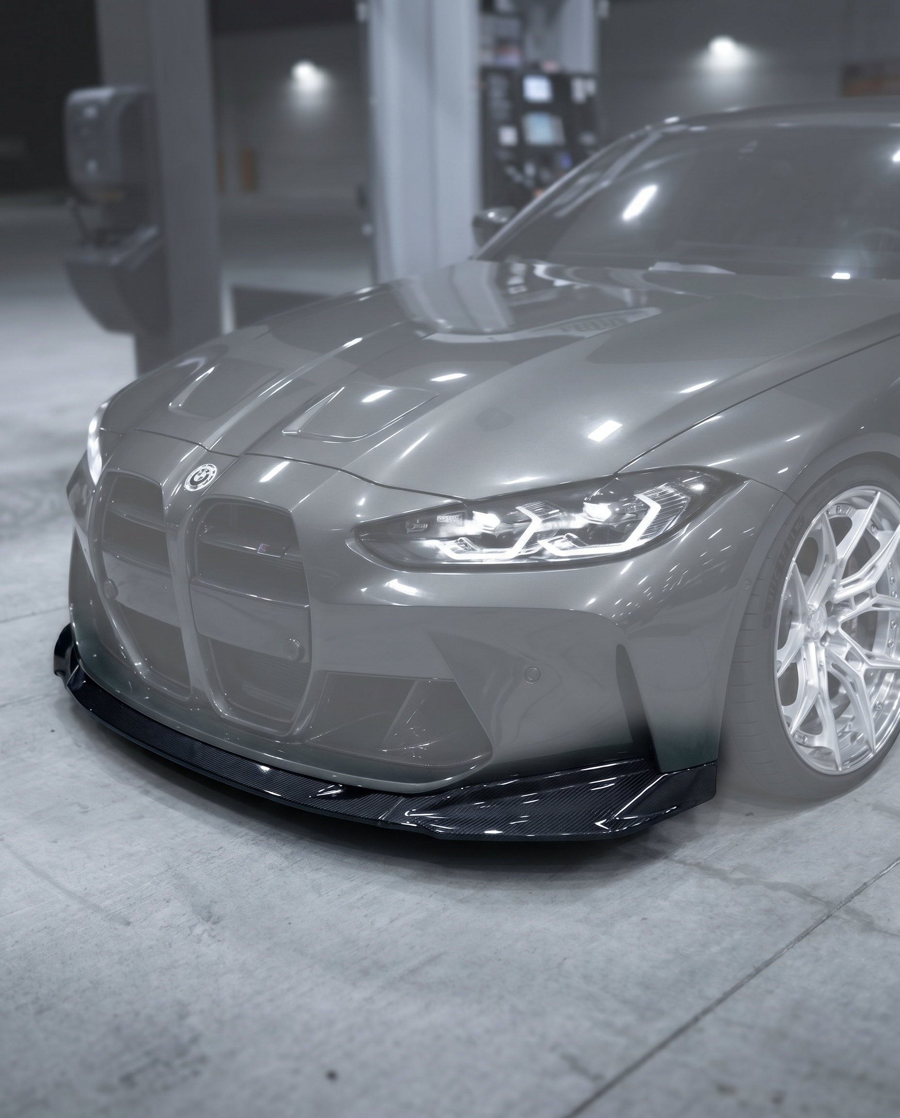 Gloss dry carbon front lip installed on BMW G80 M3 bumper, vehicle ghosted in blurred premium garage, OEM+ fitment shown sharp