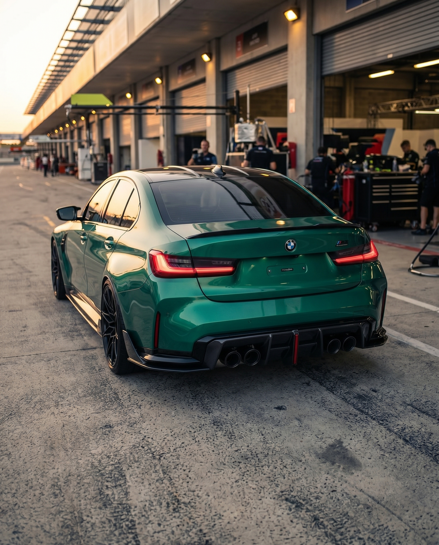 BMW G80 M3 rear 3/4 at dusk with gloss carbon V4 fin diffuser, low raking light, aggressive lowered motorsport stance