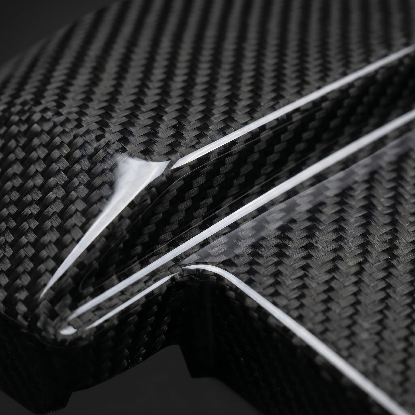 Macro of gloss 2x2 twill carbon weave on BMW dry carbon battery terminal cover, clean light-bar reflection and machined edge detail