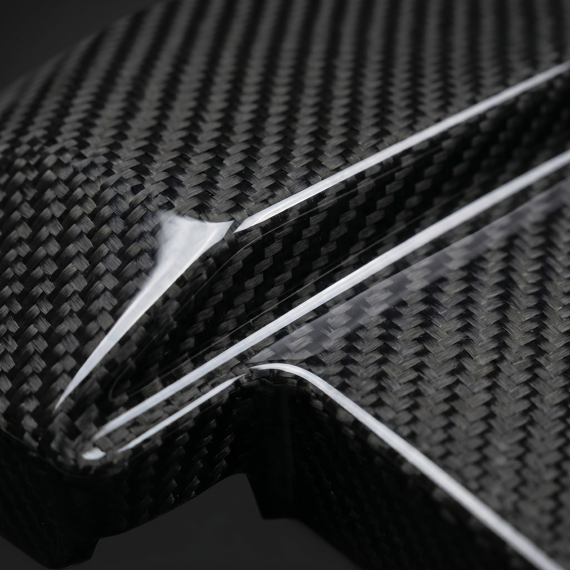Macro of gloss 2x2 twill carbon weave on BMW dry carbon battery terminal cover, clean light-bar reflection and machined edge detail