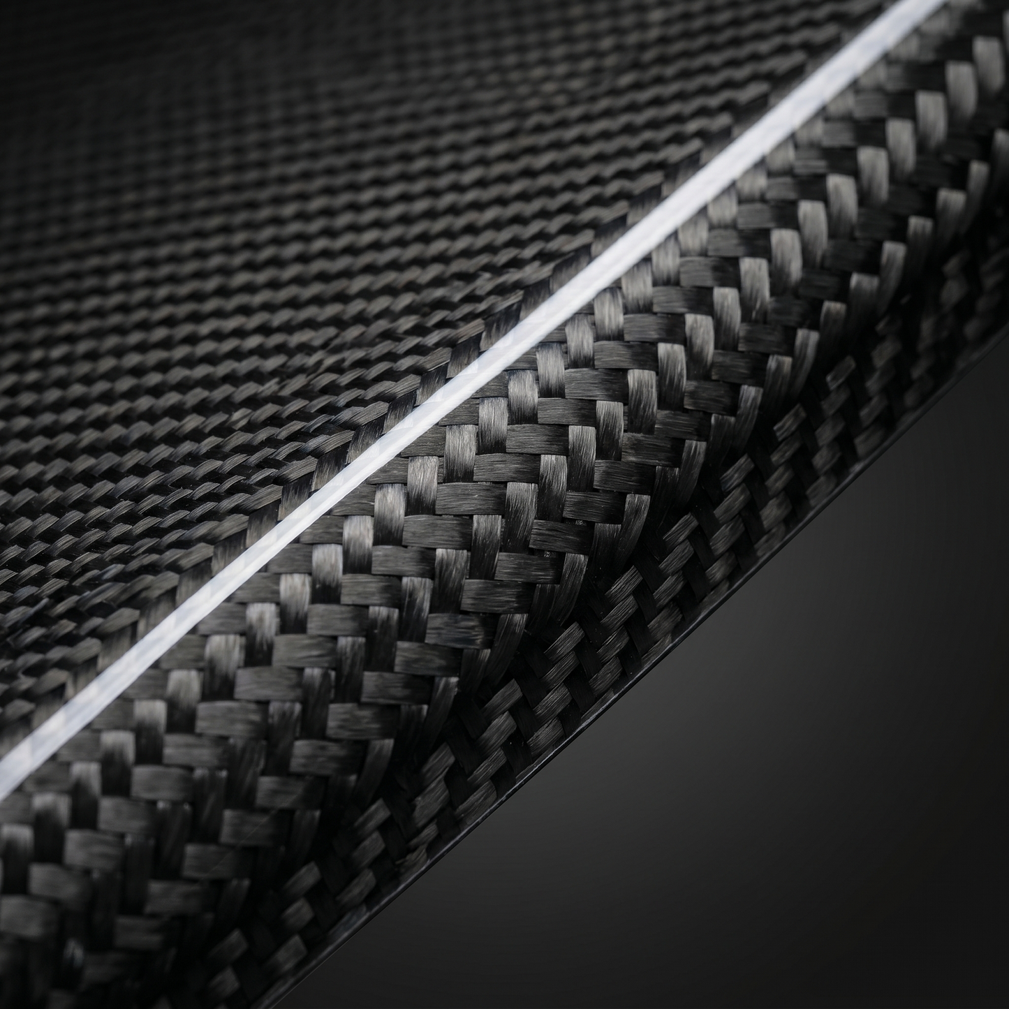 Macro of gloss 2x2 twill carbon weave on BMW dry carbon air intake cover, clean light-bar reflection and machined edge detail