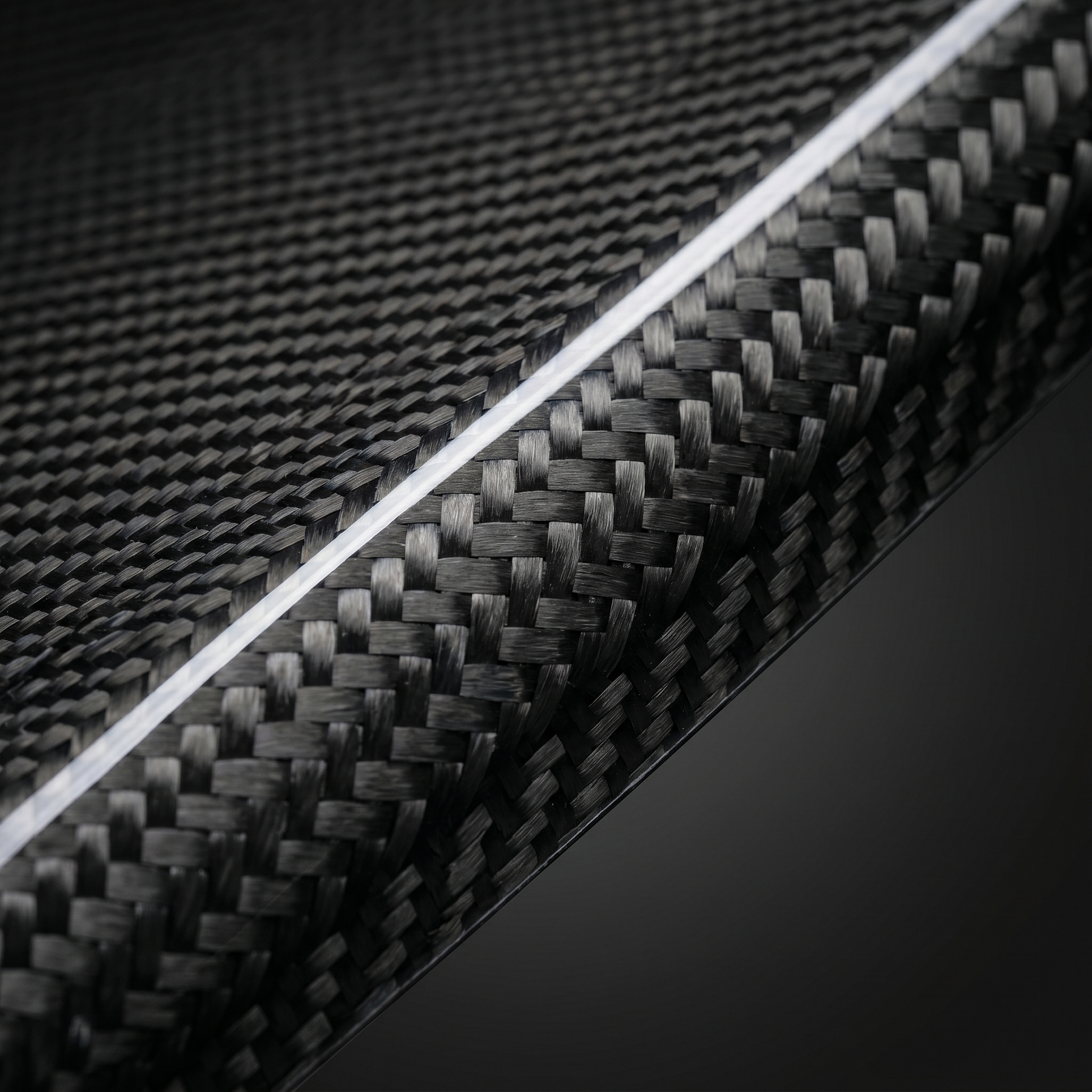 Macro of gloss 2x2 twill carbon weave on BMW dry carbon air intake cover, clean light-bar reflection and machined edge detail