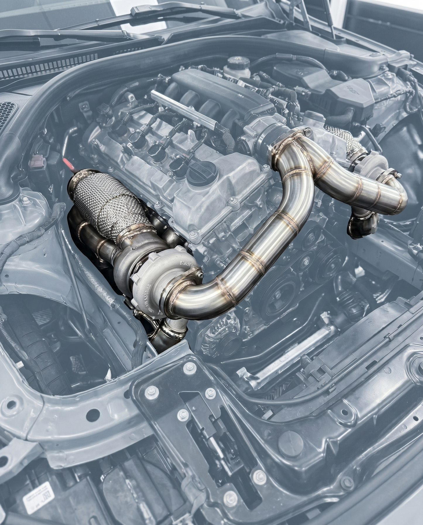 Catted stainless downpipes bolted to turbos of ghosted BMW S58 engine, polished tubing and weld beads, OEM V-band fitment shown
