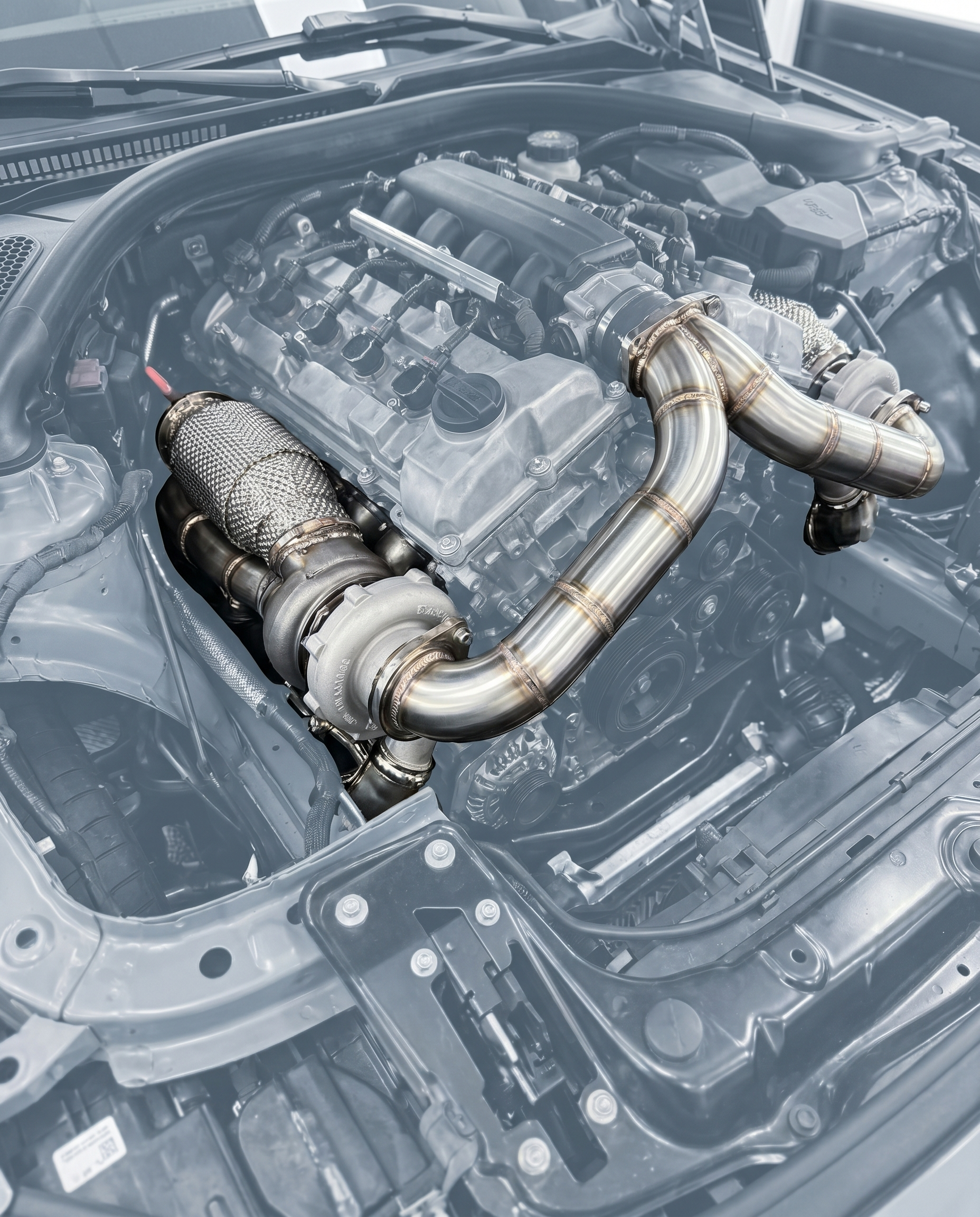 Catted stainless downpipes bolted to turbos of ghosted BMW S58 engine, polished tubing and weld beads, OEM V-band fitment shown