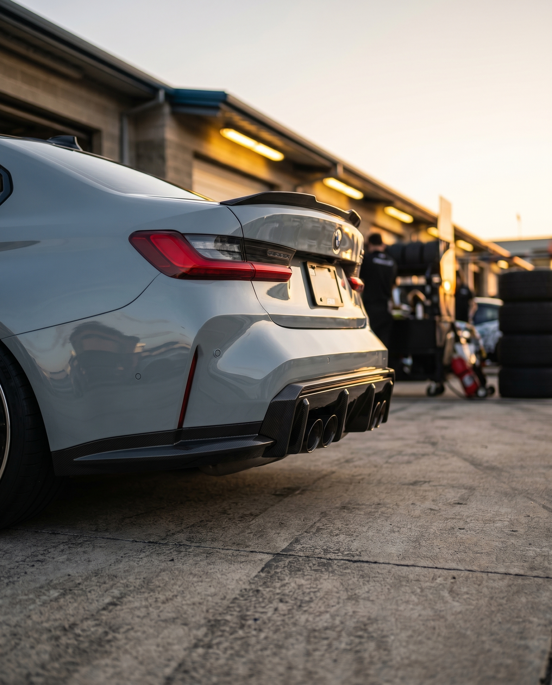 BMW G80 M3 rear 3/4 at dusk with 3D layered carbon rear diffuser, warm raking light, aggressive lowered motorsport stance