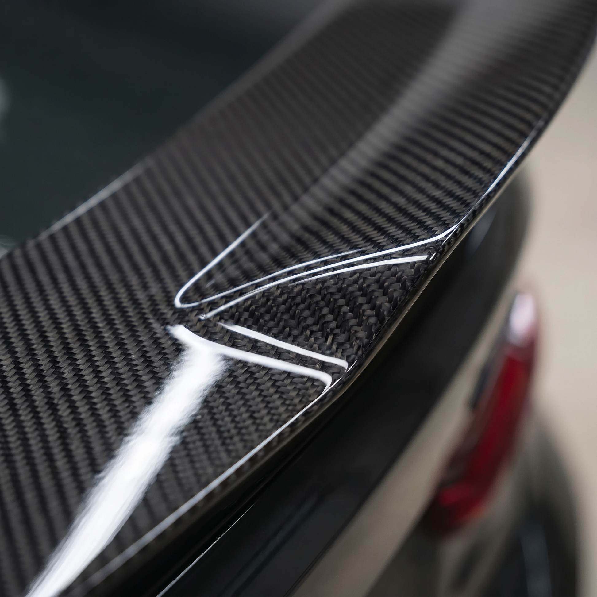 Macro of gloss 2x2 twill weave on V-style carbon trunk spoiler for BMW G8X, showing clear-coat depth and machined edge