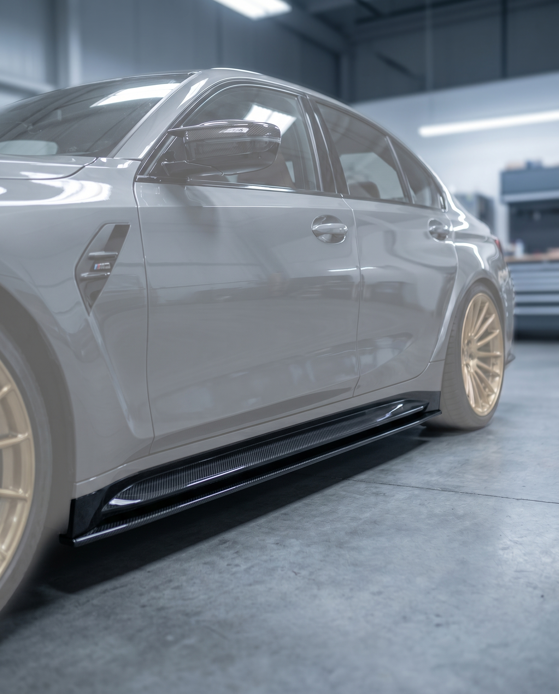 Gloss carbon side skirt extension installed along the rocker of BMW G80 M3, premium garage lighting shows lowered stance