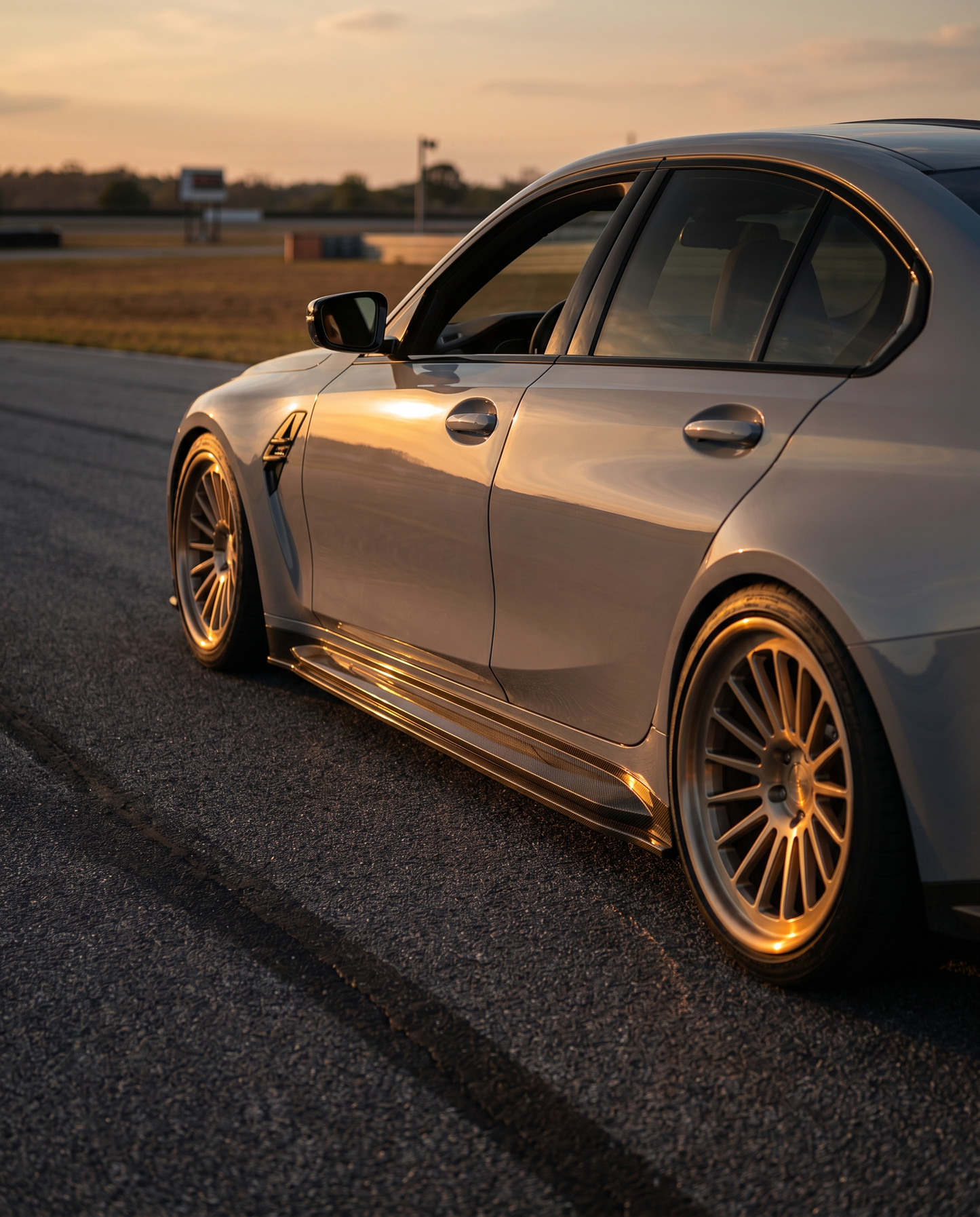 BMW G80 M3 at golden-hour dusk with carbon side skirt extensions, low side 3/4 view emphasizing the planted stance