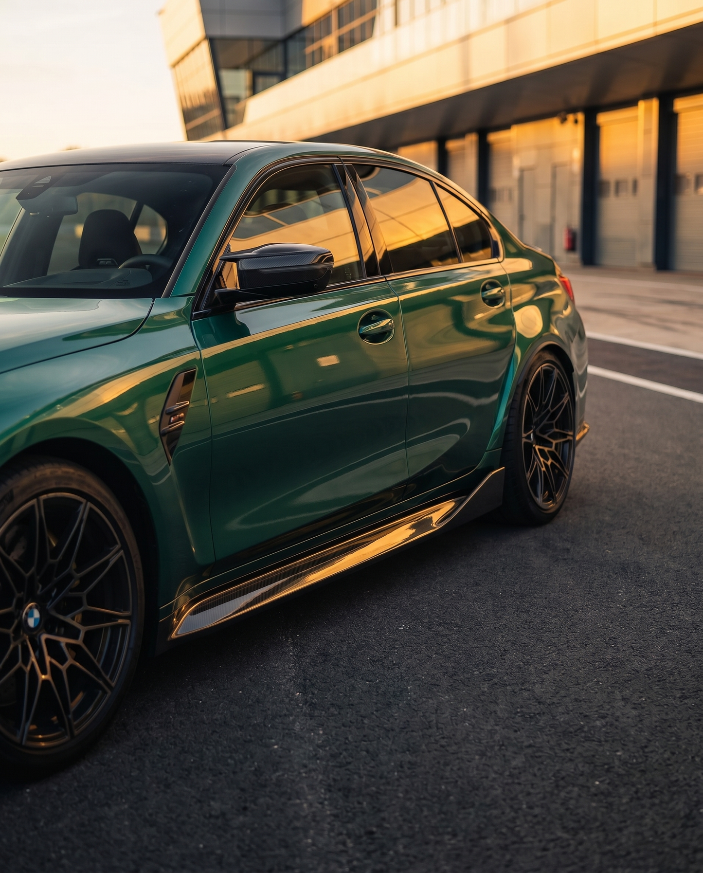 BMW G80 M3 at golden-hour dusk with MP-style carbon side skirts, low side 3/4 view emphasizing planted stance