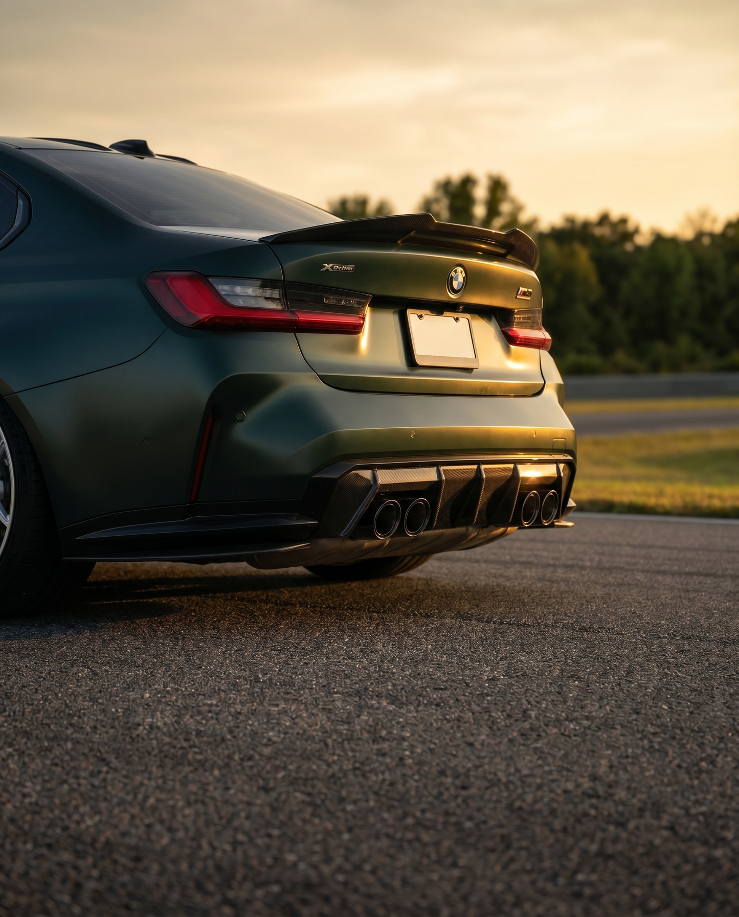 BMW G80 M3 at golden-hour dusk with MP-style carbon rear diffuser, rear 3/4 low view finishing the aero