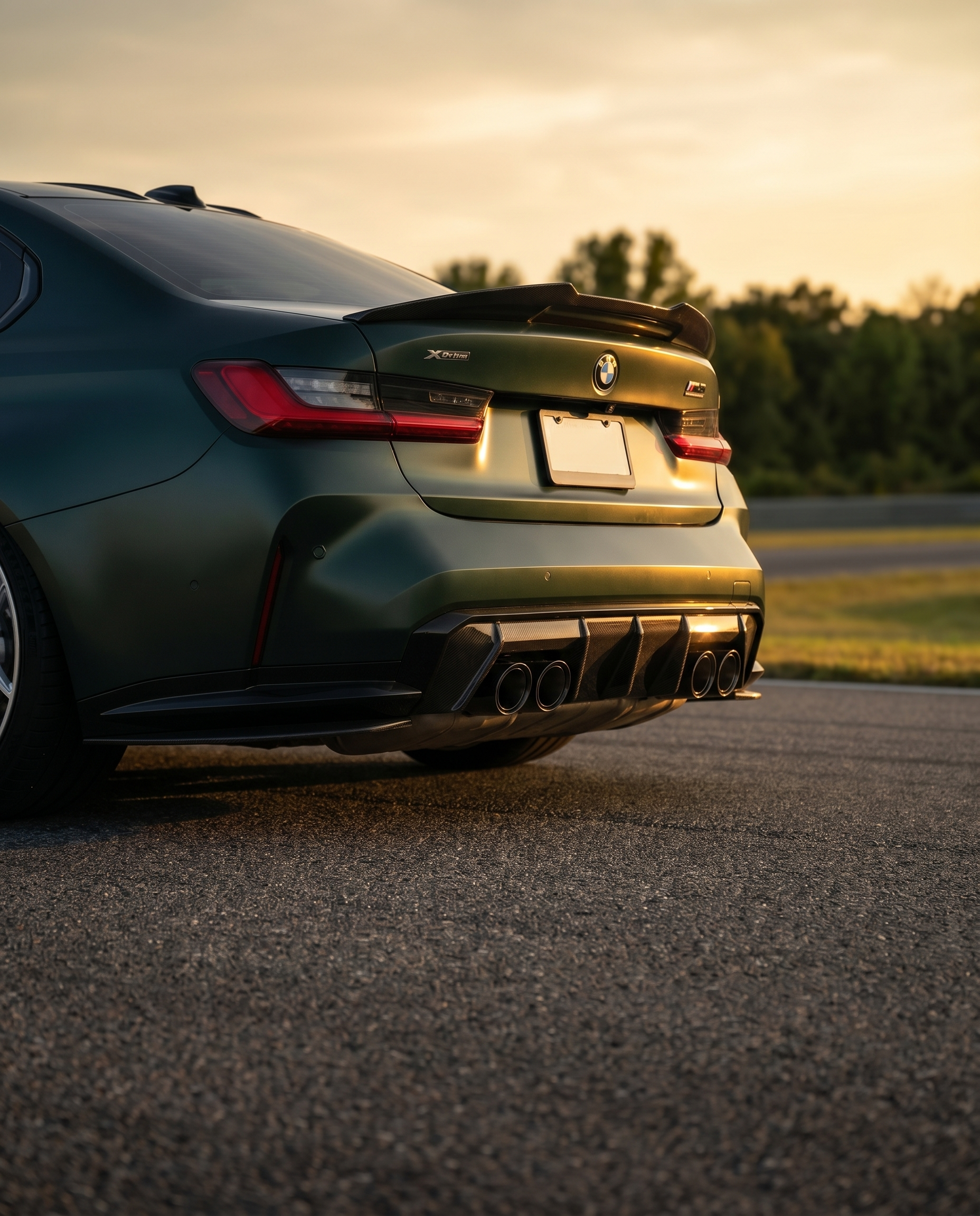 BMW G80 M3 at golden-hour dusk with MP-style carbon rear diffuser, rear 3/4 low view finishing the aero