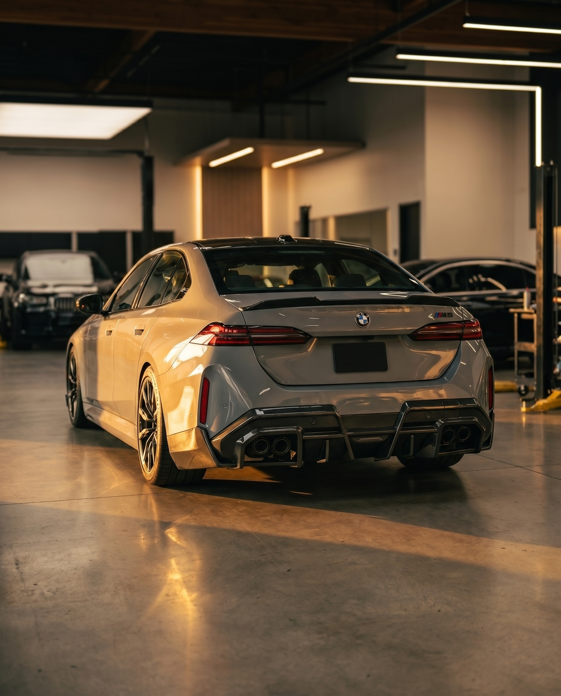 BMW G90 M5 at golden-hour dusk with SQ-style F1-inspired carbon rear diffuser, rear 3/4 low view anchoring the aero