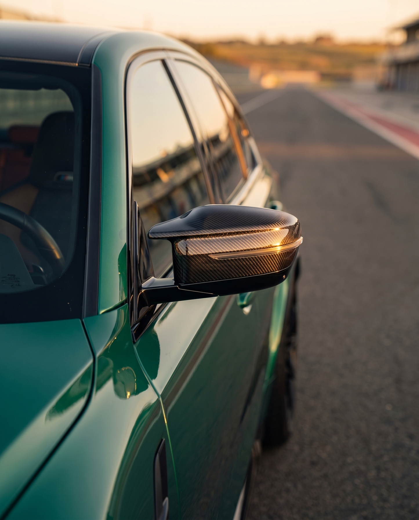 BMW G80 M3 at golden-hour dusk with gloss carbon mirror cap, tight side detail catching warm light