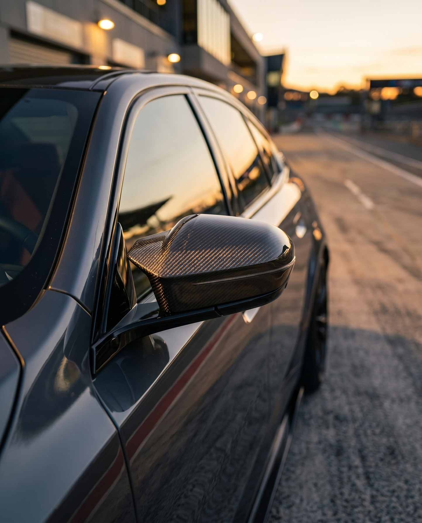 BMW G90 M5 at golden-hour dusk with gloss carbon mirror cover, tight side detail catching warm light