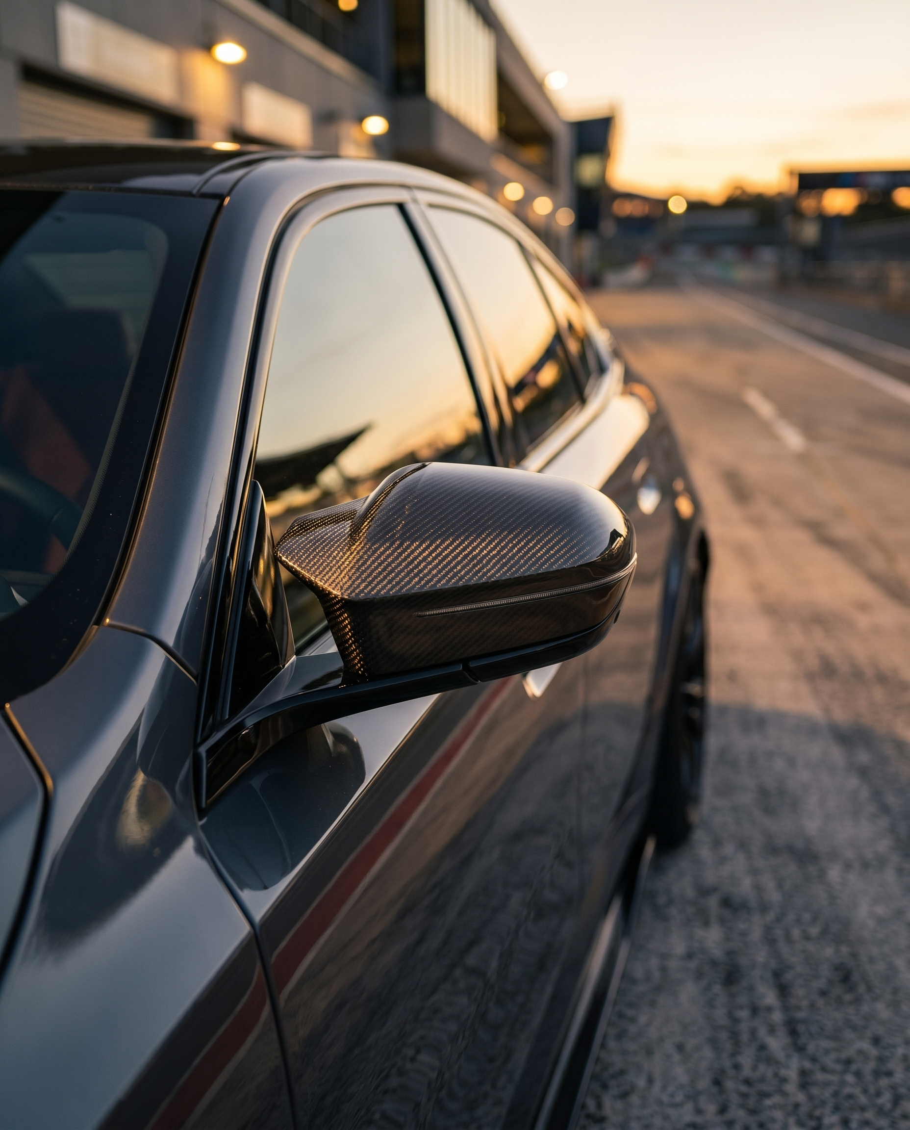 BMW G90 M5 at golden-hour dusk with gloss carbon mirror cover, tight side detail catching warm light