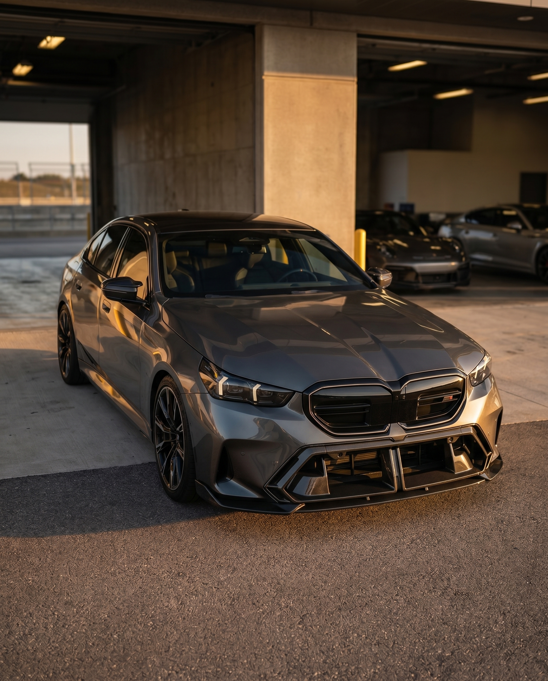 BMW G90 M5 at golden-hour dusk with OE-style dry carbon front center vent, front 3/4 view with refined factory look